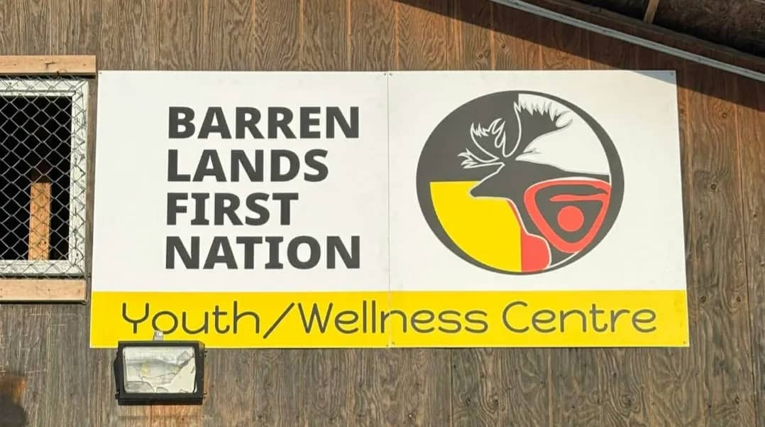 Barren Lands First Nation Youth/Wellness Centre sign with the Nation's logo, mounted on the building's wood siding