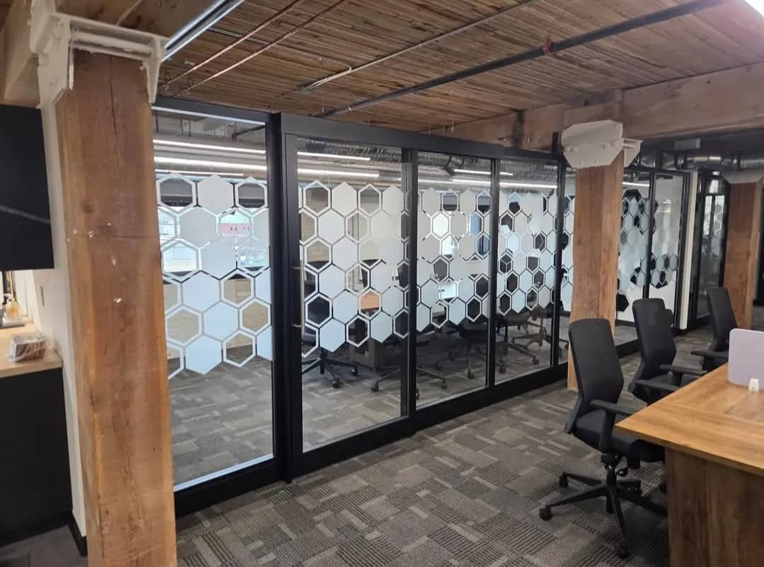 Meeting room glass walls finished with a frosted hexagon pattern window film for privacy, in an office with exposed wood beams