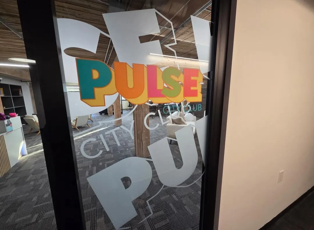 Frosted window etch with large PULSE and City Club lettering on a glass office door, with a full colour Pulse logo decal, at a Saskatoon co-working space