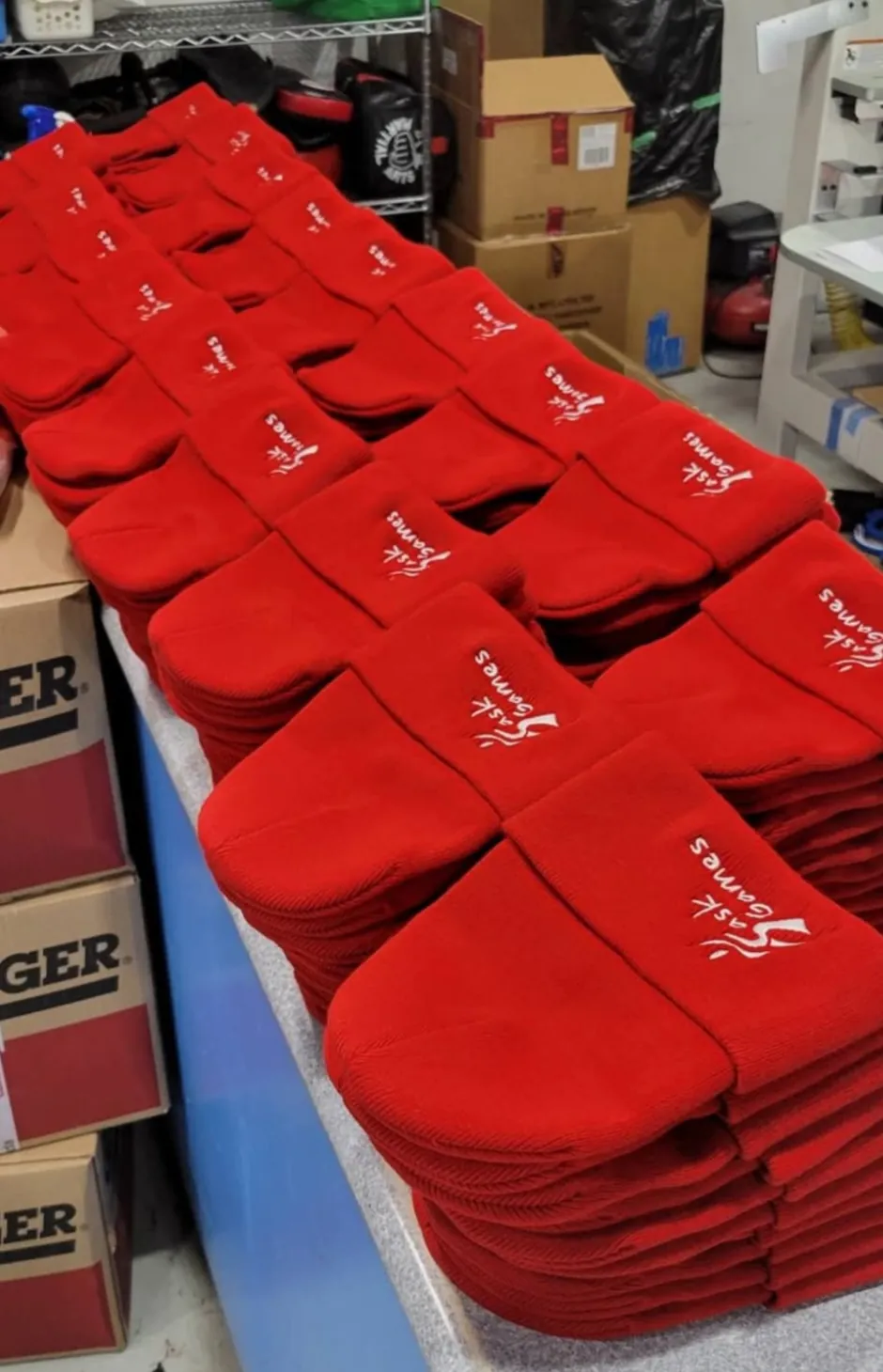 Stacks of red toques with a white Sask Games logo lined up on a work table