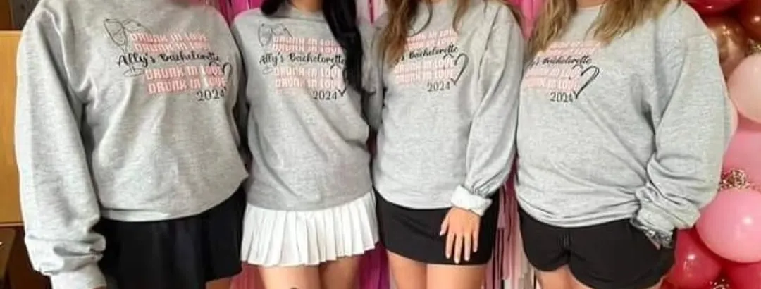 Four matching grey crewneck sweaters printed with a custom bachelorette party design in pink and black