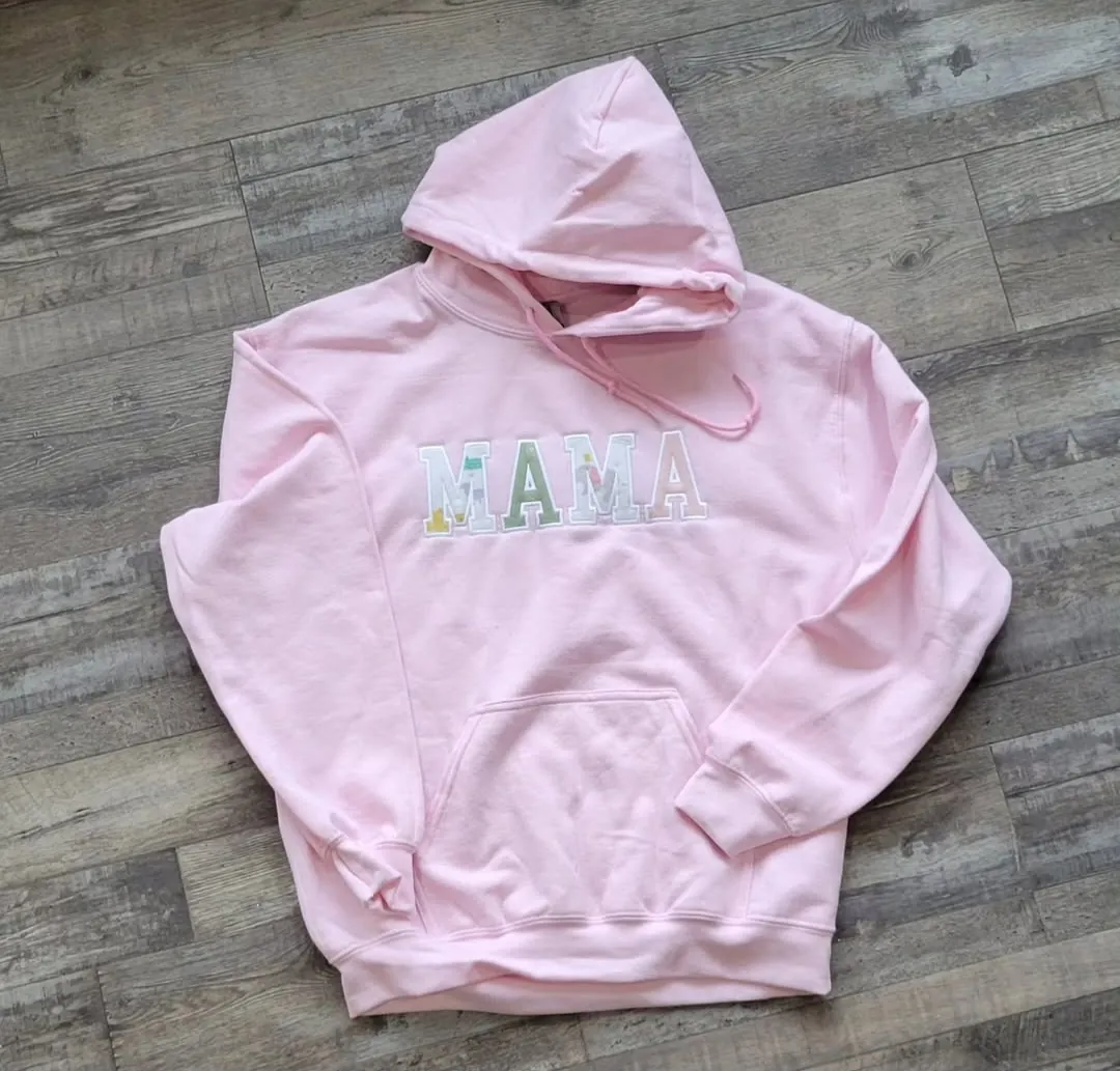 Light pink hoodie with MAMA lettering on the chest, each letter made from a different patterned fabric