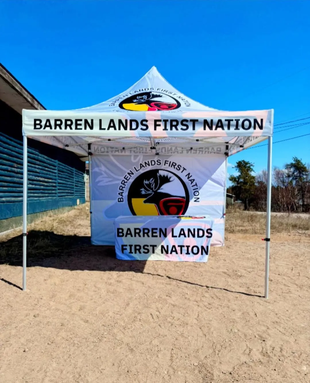 Custom printed 10x10 pop-up tent with full back wall and a fitted table cloth, all branded for Barren Lands First Nation, set up outdoors