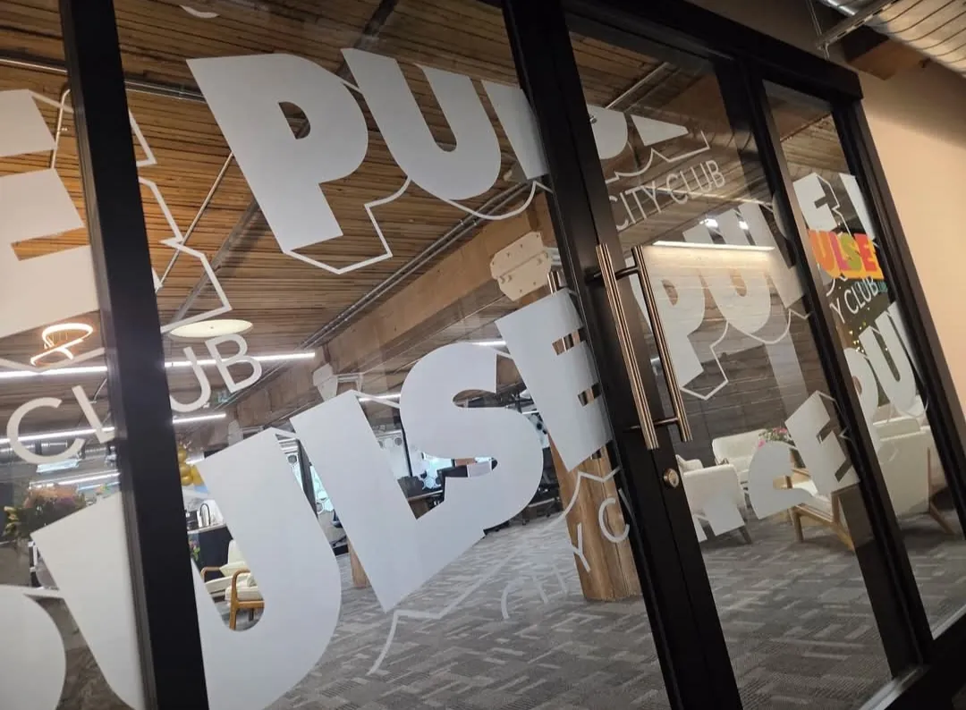 Glass wall and doors covered in frosted etch film with oversized PULSE City Club lettering, looking into the co-working lounge